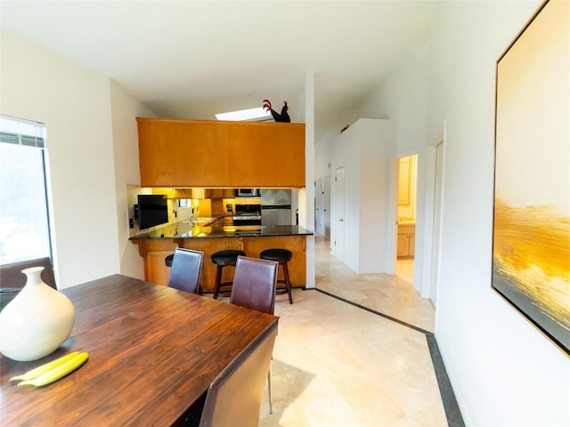 kitchen featuring kitchen peninsula, stainless steel fridge, vaulted ceiling, and a breakfast bar area