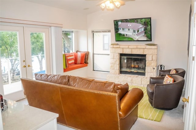 living room featuring ceiling fan, a stone fireplace, and french doors