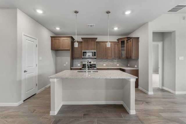 kitchen with light stone countertops, sink, stainless steel appliances, an island with sink, and pendant lighting