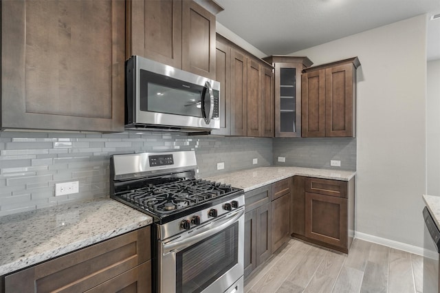 kitchen with dark brown cabinetry, appliances with stainless steel finishes, tasteful backsplash, light wood-type flooring, and light stone counters