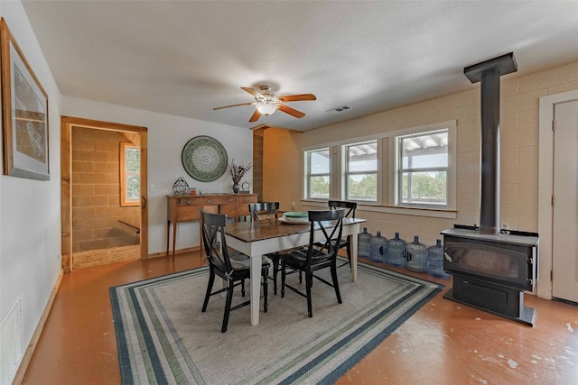 dining room featuring a textured ceiling, concrete floors, ceiling fan, and a wood stove