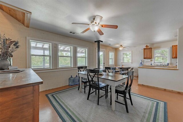 dining area with a wood stove, a healthy amount of sunlight, ceiling fan, and a textured ceiling