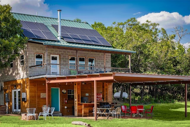 rear view of property featuring a lawn, solar panels, and a balcony