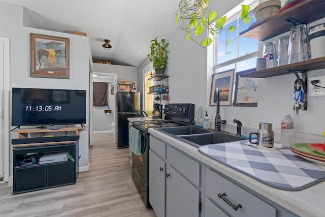 kitchen with white cabinets, sink, light hardwood / wood-style floors, black appliances, and vaulted ceiling