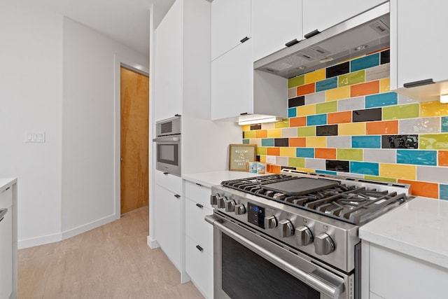 kitchen with white cabinets, decorative backsplash, light stone counters, light hardwood / wood-style floors, and stainless steel appliances