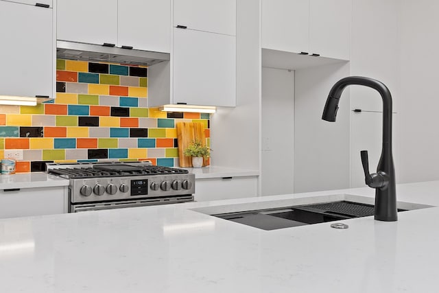 kitchen with sink, backsplash, gas stove, and white cabinets