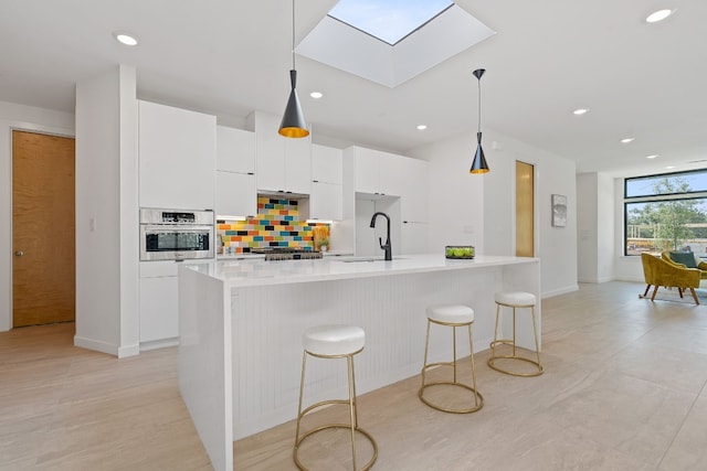 kitchen with stainless steel appliances, white cabinetry, an island with sink, and decorative light fixtures