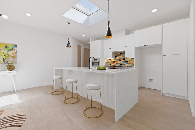 kitchen with pendant lighting, white cabinetry, a skylight, a center island with sink, and decorative backsplash