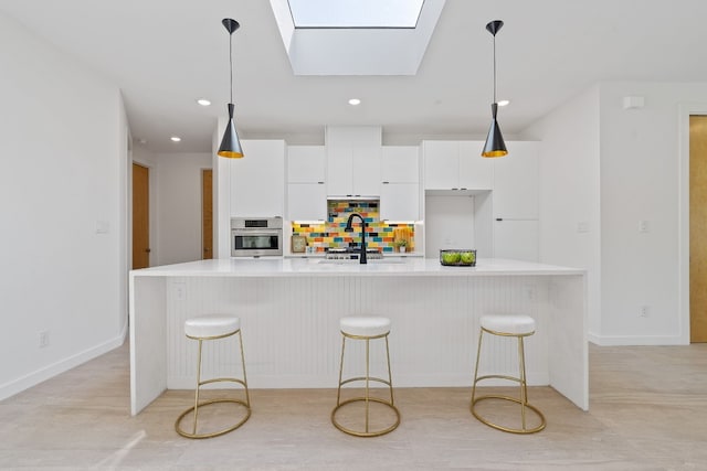 kitchen featuring pendant lighting, a skylight, sink, stainless steel oven, and a center island with sink