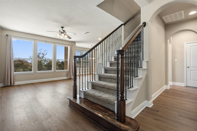 stairs with a textured ceiling, ceiling fan, and dark hardwood / wood-style floors