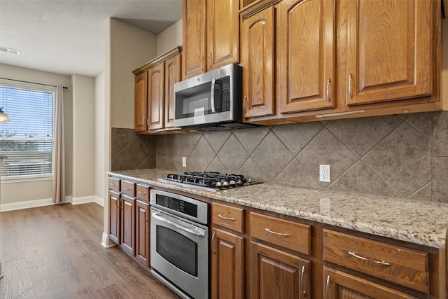 kitchen featuring appliances with stainless steel finishes, backsplash, dark hardwood / wood-style floors, and light stone countertops