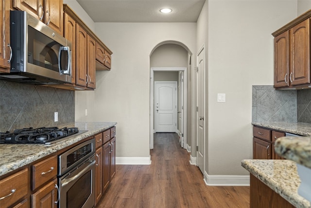 kitchen featuring light stone countertops, backsplash, dark hardwood / wood-style flooring, and stainless steel appliances