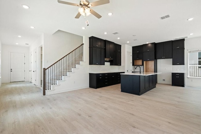 kitchen featuring tasteful backsplash, ceiling fan, a center island with sink, and light wood-type flooring