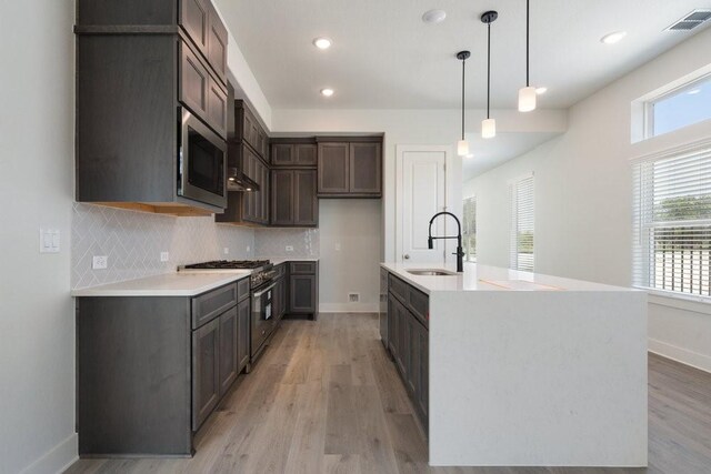 kitchen with visible vents, a sink, decorative backsplash, stainless steel appliances, and light wood-style floors