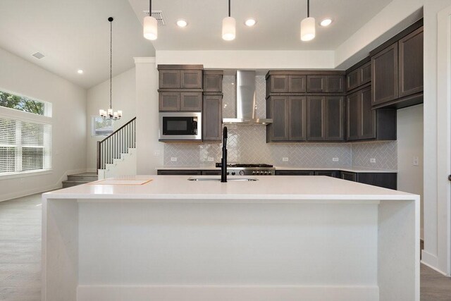 kitchen with stainless steel microwave, dark brown cabinets, light countertops, and wall chimney range hood