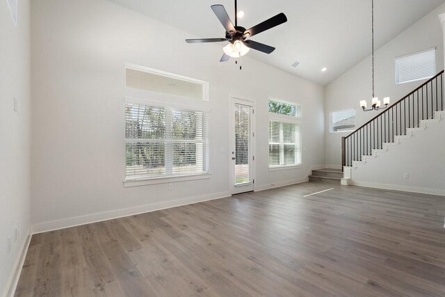 entryway with baseboards, stairway, ceiling fan with notable chandelier, wood finished floors, and high vaulted ceiling