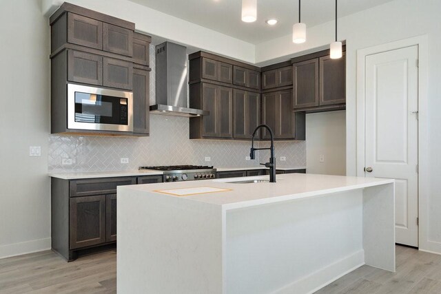 kitchen with a sink, light countertops, light wood-style floors, stainless steel microwave, and wall chimney exhaust hood