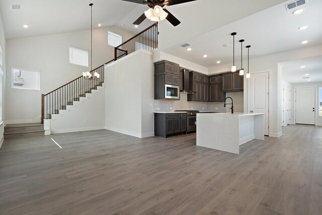 kitchen with wall chimney range hood, open floor plan, light wood finished floors, and stainless steel appliances