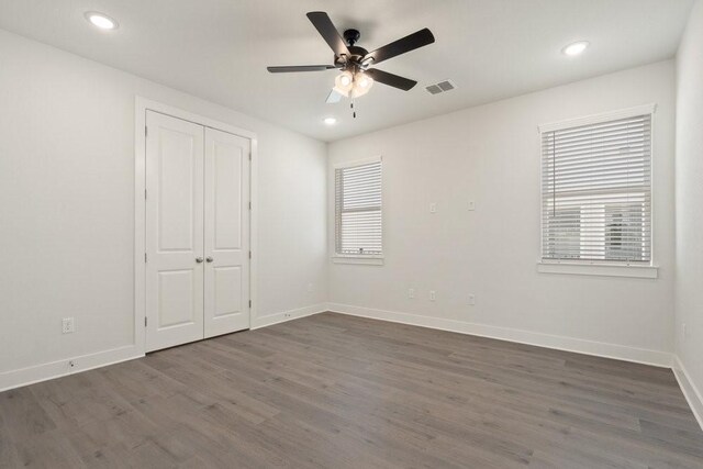 unfurnished bedroom with visible vents, multiple windows, dark wood-style floors, and baseboards