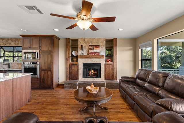 living room with dark hardwood / wood-style flooring, plenty of natural light, a tiled fireplace, and ceiling fan