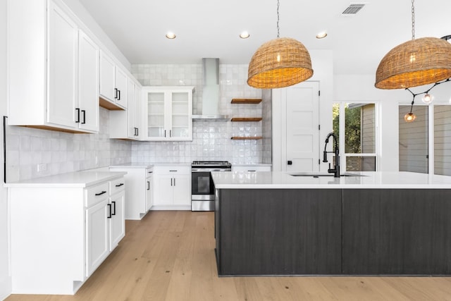 kitchen featuring wall chimney exhaust hood, sink, stainless steel range oven, white cabinets, and an island with sink