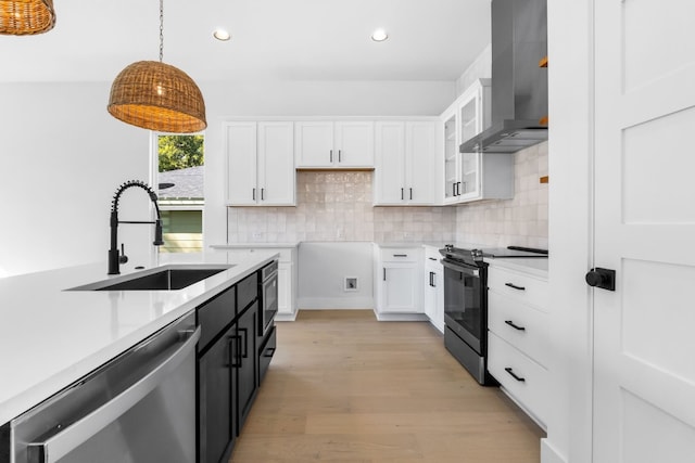 kitchen with appliances with stainless steel finishes, wall chimney exhaust hood, sink, white cabinets, and hanging light fixtures