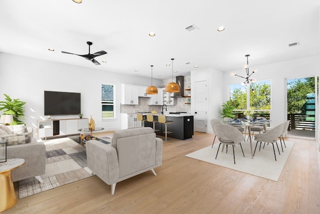 living room with light wood-type flooring, ceiling fan with notable chandelier, and sink