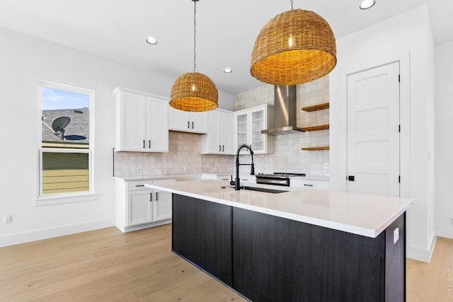 kitchen with sink, white cabinets, pendant lighting, and wall chimney range hood