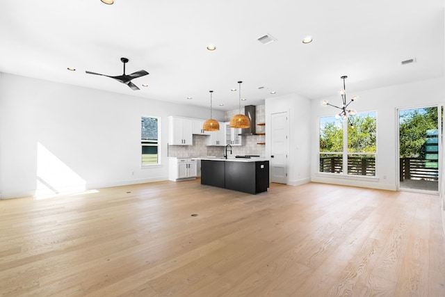 unfurnished living room with ceiling fan with notable chandelier, sink, and light hardwood / wood-style flooring