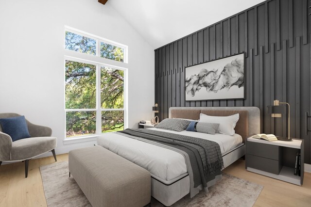 bedroom with beam ceiling, high vaulted ceiling, and light hardwood / wood-style flooring