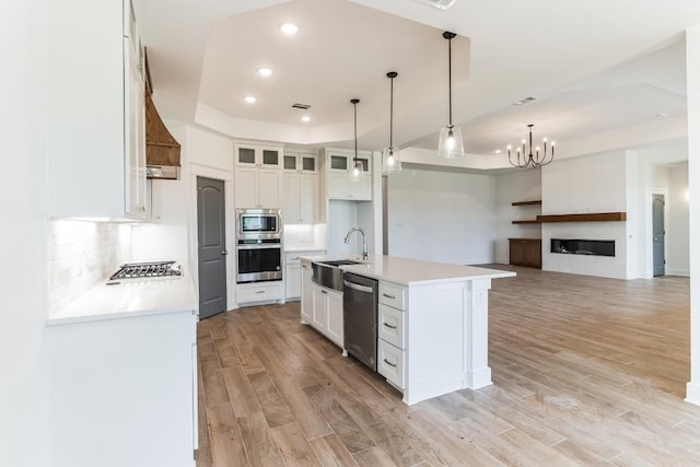 kitchen with appliances with stainless steel finishes, white cabinetry, an island with sink, sink, and a tray ceiling