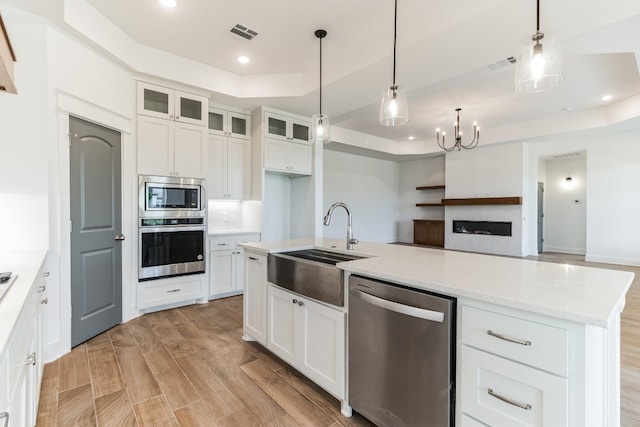 kitchen with appliances with stainless steel finishes, pendant lighting, light hardwood / wood-style floors, white cabinetry, and a raised ceiling