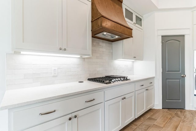 kitchen with light stone countertops, stainless steel gas cooktop, white cabinets, and premium range hood