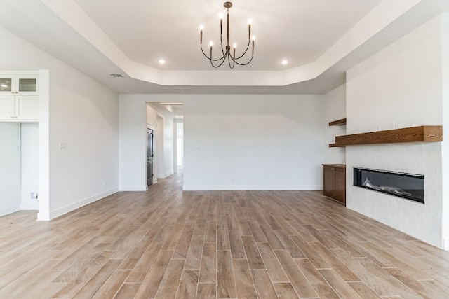 unfurnished living room featuring a notable chandelier, light hardwood / wood-style floors, and a raised ceiling