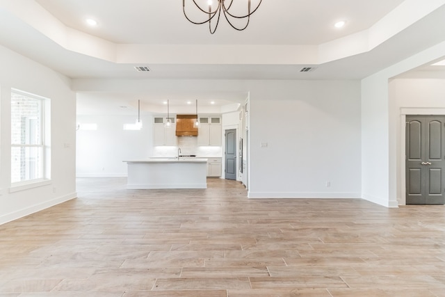 unfurnished living room with a raised ceiling, sink, a chandelier, and light hardwood / wood-style flooring