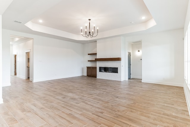 unfurnished living room featuring a raised ceiling, a notable chandelier, and light hardwood / wood-style floors