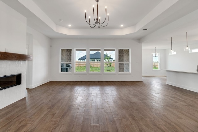 unfurnished living room with dark hardwood / wood-style flooring, a fireplace, a raised ceiling, and a chandelier