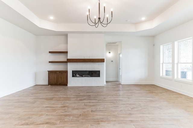 unfurnished living room with a tray ceiling, a chandelier, and light hardwood / wood-style floors