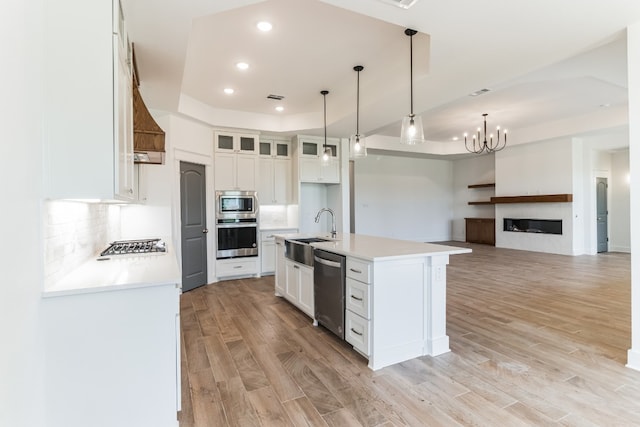 kitchen with sink, appliances with stainless steel finishes, a tray ceiling, a kitchen island with sink, and white cabinets