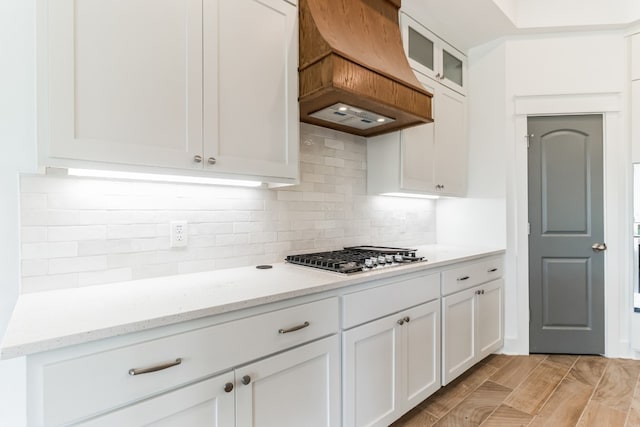 kitchen featuring stainless steel gas stovetop, light stone countertops, custom range hood, and white cabinets