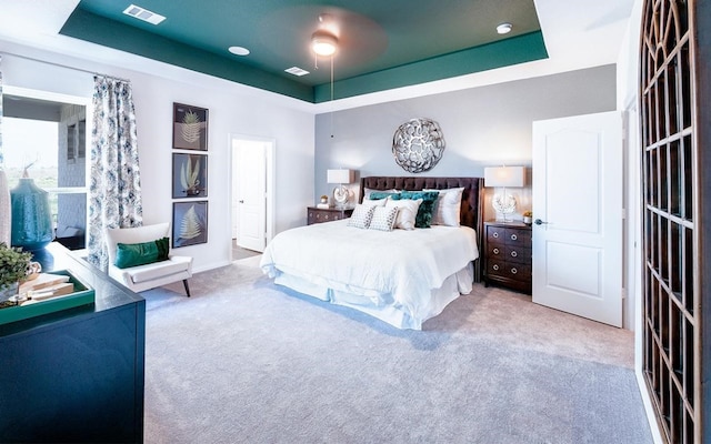 bedroom with ceiling fan, light carpet, and a tray ceiling