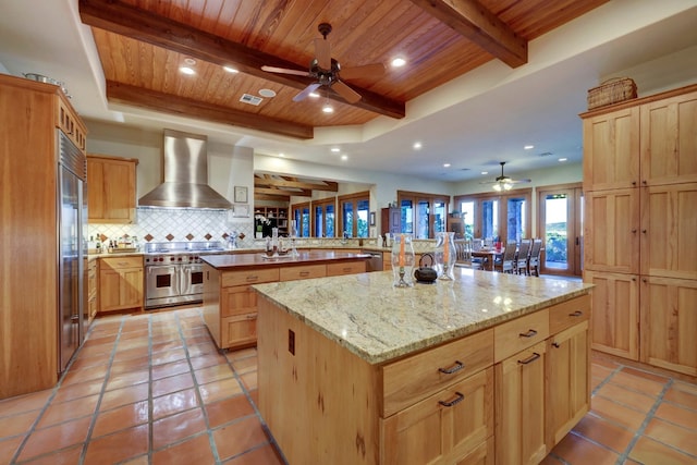 kitchen with a center island with sink, ceiling fan, wooden ceiling, and wall chimney range hood