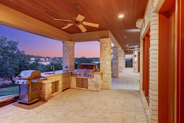 patio terrace at dusk with area for grilling, an outdoor kitchen, ceiling fan, and sink