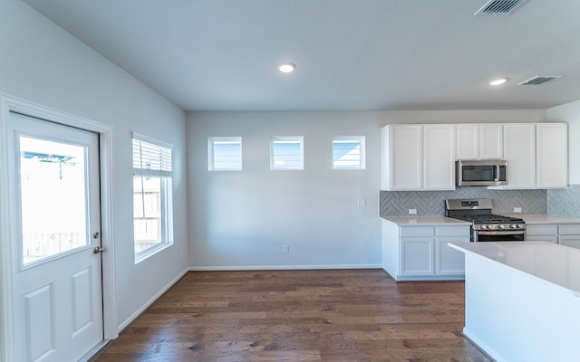 kitchen featuring stainless steel appliances, tasteful backsplash, dark wood-type flooring, and white cabinetry