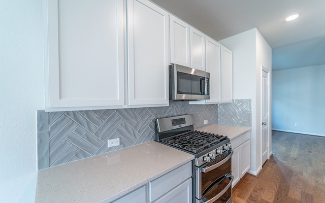 kitchen with dark wood-type flooring, appliances with stainless steel finishes, white cabinets, backsplash, and light stone counters