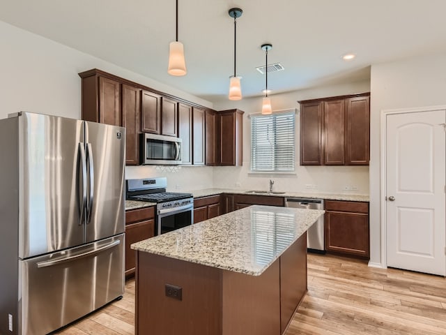 kitchen featuring hanging light fixtures, light hardwood / wood-style flooring, stainless steel appliances, light stone counters, and a kitchen island