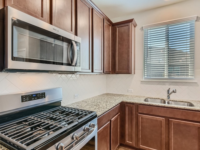 kitchen featuring light stone counters, backsplash, sink, and stainless steel appliances