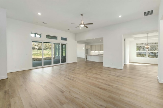 unfurnished living room featuring ceiling fan with notable chandelier, sink, and light wood-type flooring