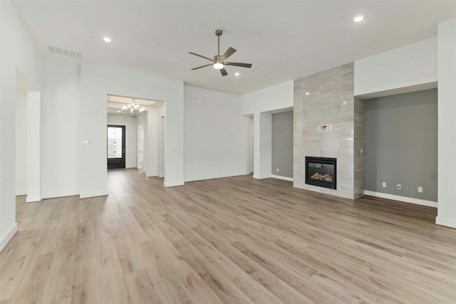 unfurnished living room featuring a tile fireplace, light wood-type flooring, ceiling fan with notable chandelier, and tile walls