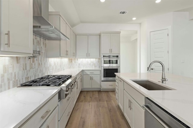 kitchen with light wood-type flooring, backsplash, stainless steel appliances, wall chimney exhaust hood, and sink